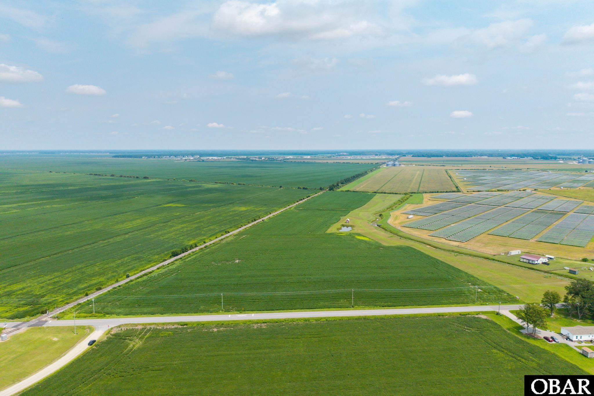 Aerial view of expansive green farmland and a large solar panel array beside a road.