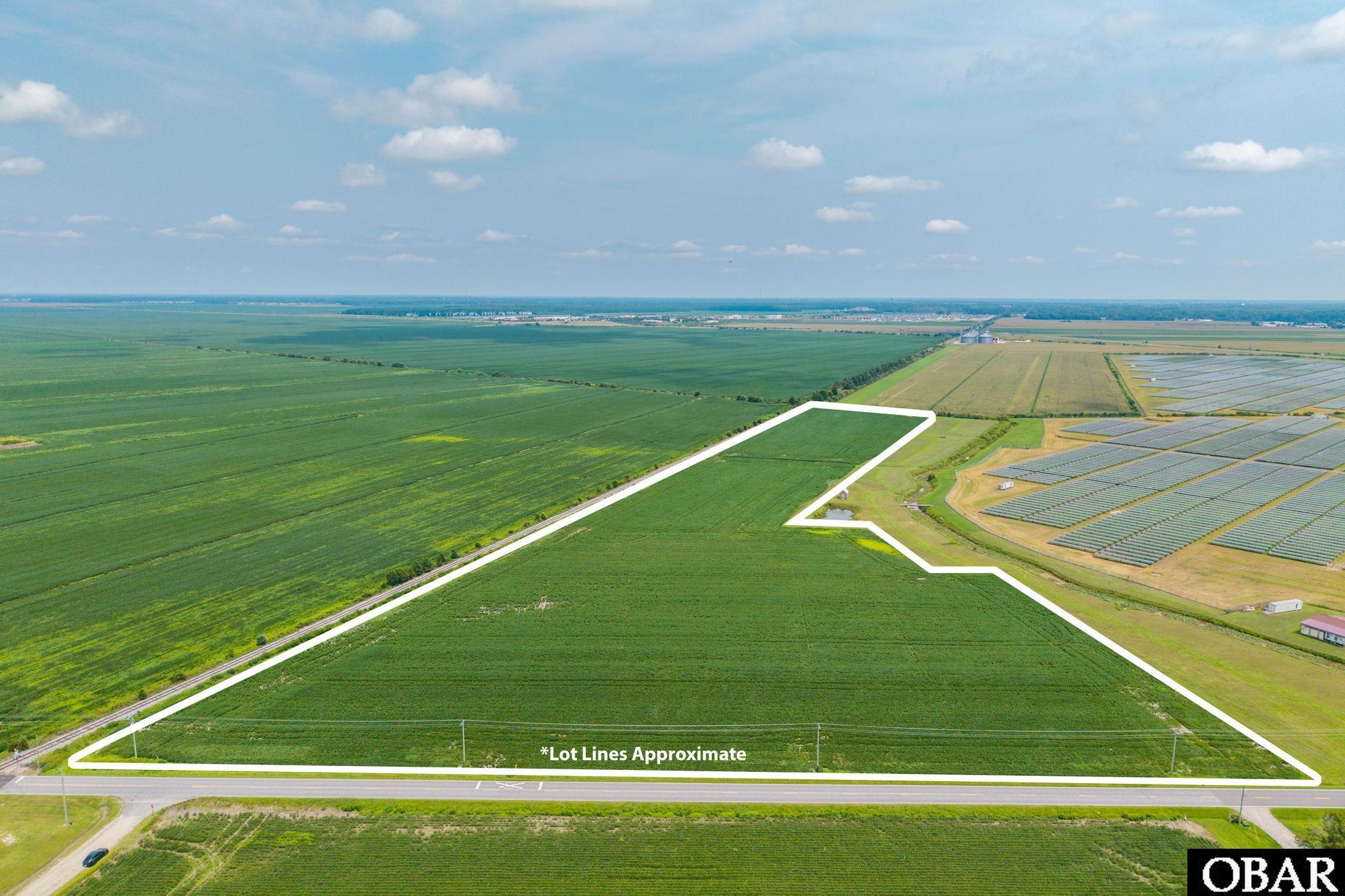 Aerial view of cultivated land outlined along a road, with neighboring fields and solar panels.
