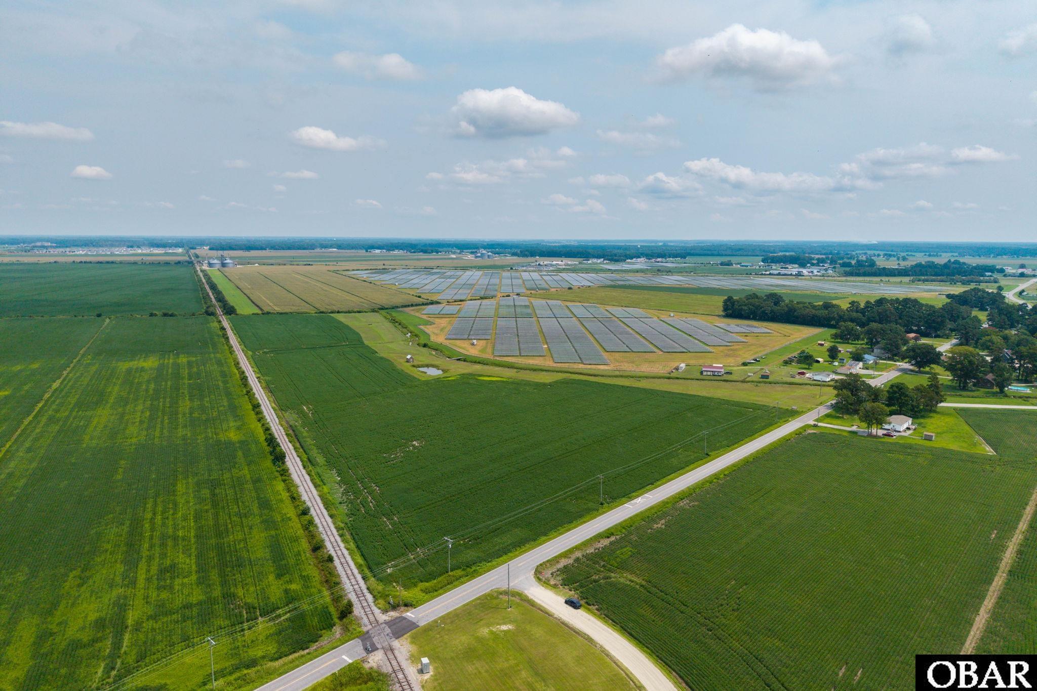 Aerial farmland with a large solar panel array, railroad tracks, and roads.