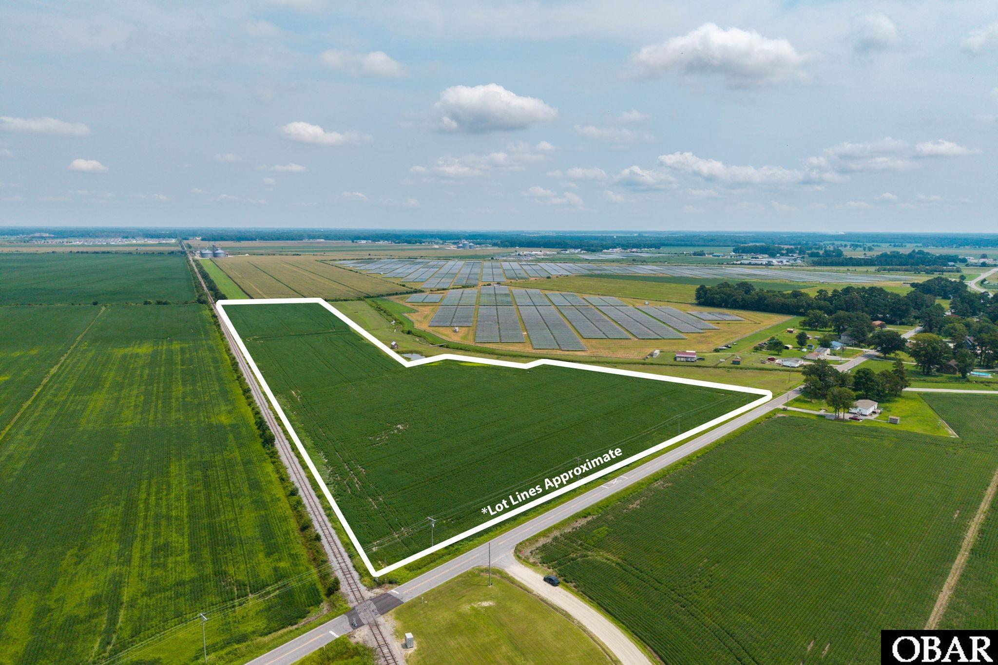 Aerial view of outlined farmland beside a road and railroad tracks, with solar panels nearby.