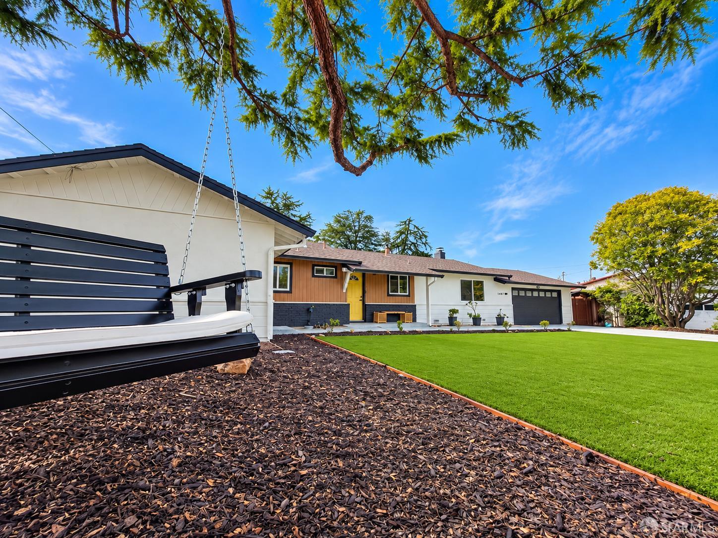 Single-story home with a yellow front door, green lawn, and hanging porch swing.