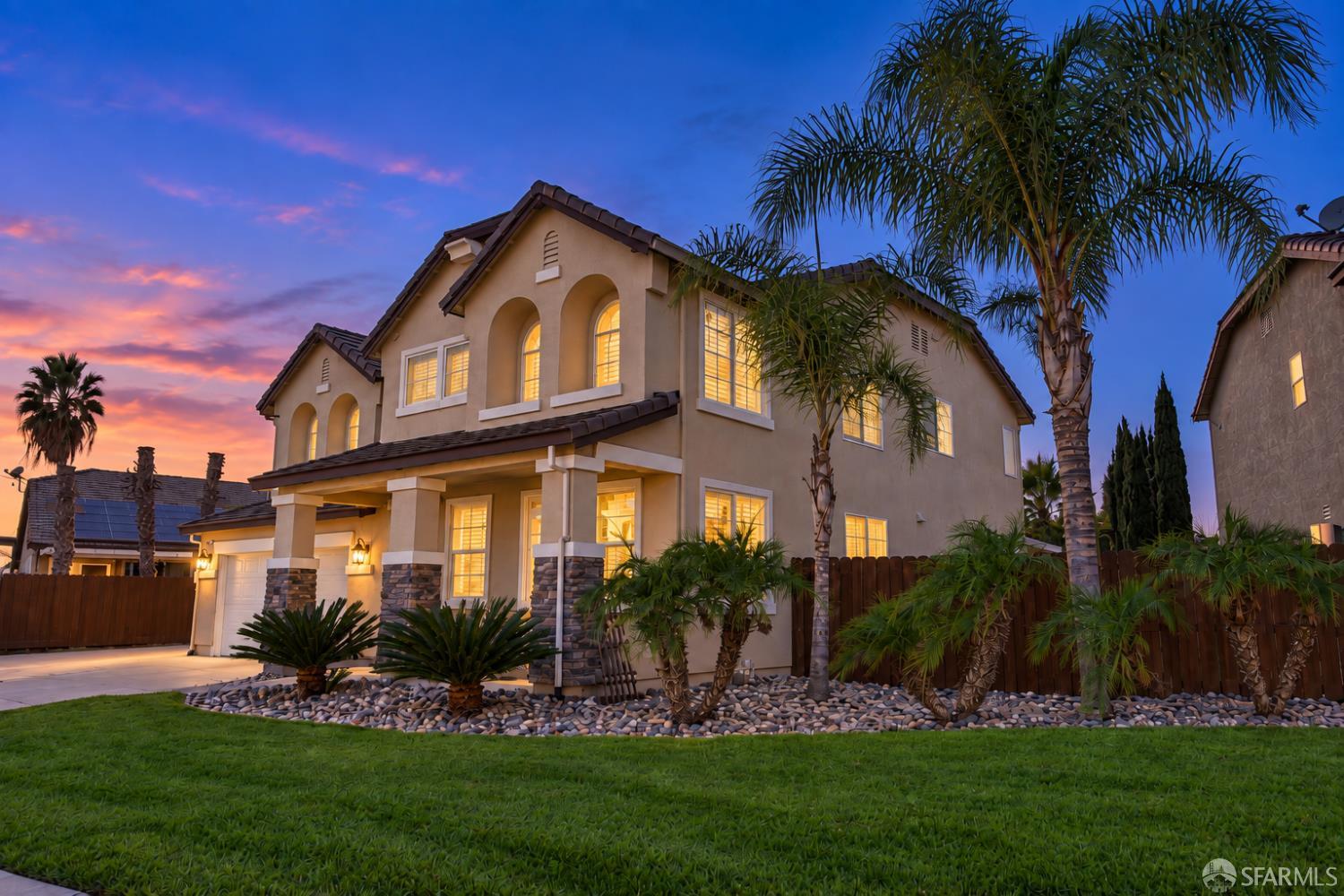Two-story stucco home with arched windows and palm trees glowing at dusk.