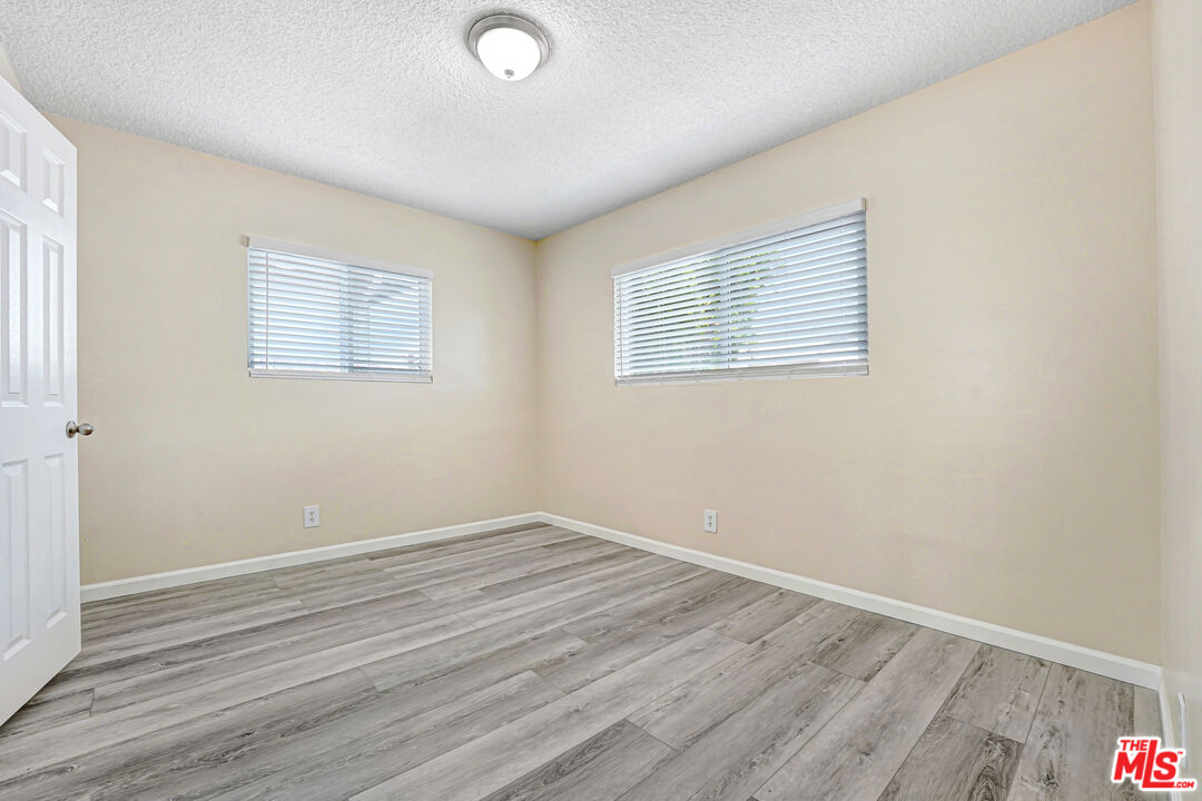Empty room with gray plank flooring, beige walls, and two windows with blinds.