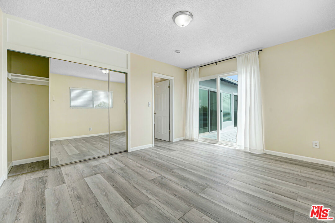 Empty bedroom with mirrored closet doors, gray tile flooring, and a sliding glass door to the patio.