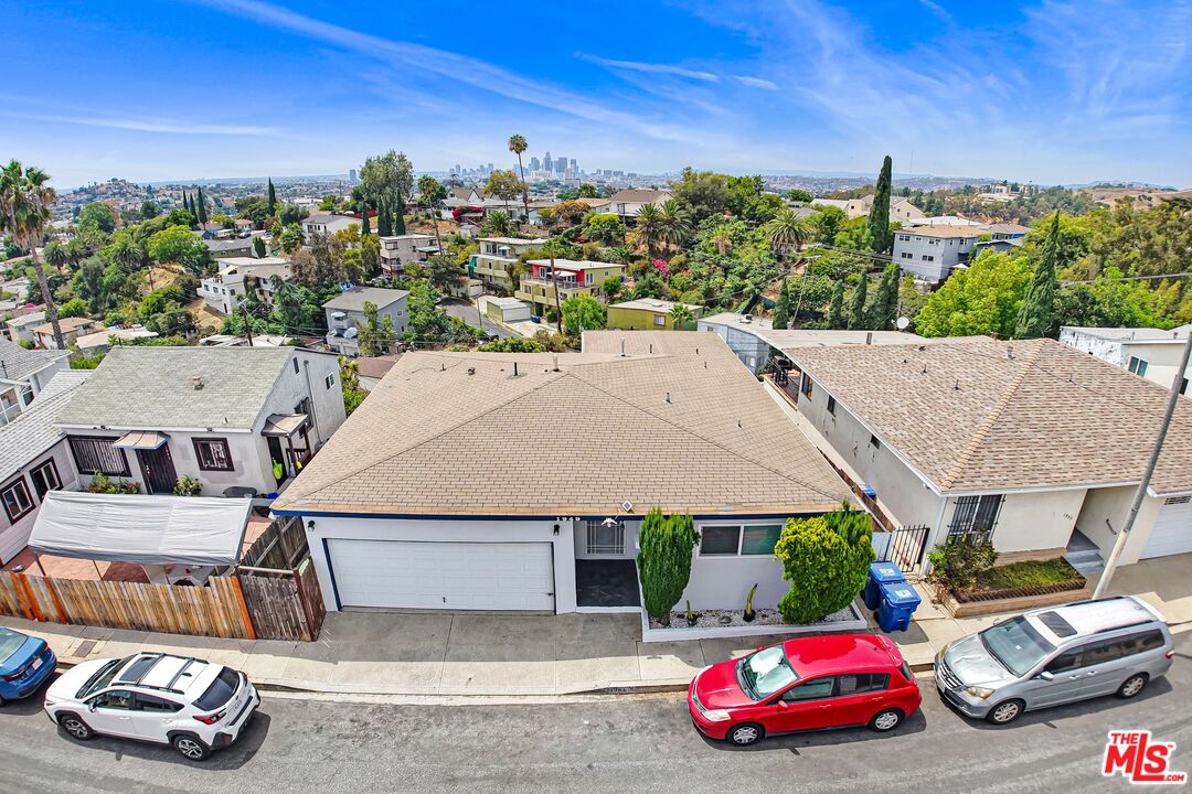 Single-story home with a tan roof and front garage, surrounded by homes with the Los Angeles skyline beyond.