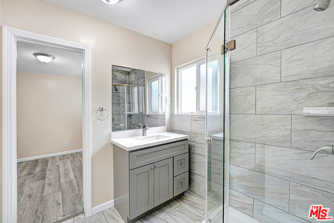 Bathroom with a gray vanity, large tiled shower, glass enclosure, and bright window.