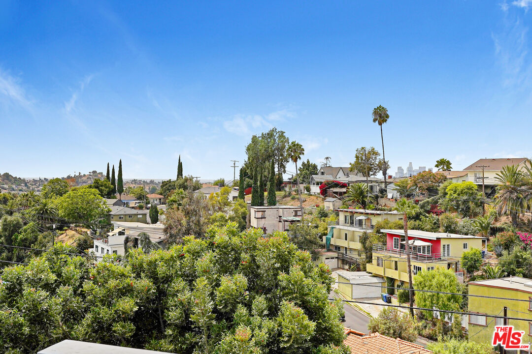 Hillside neighborhood with colorful homes, tall palms, and the distant Los Angeles skyline.