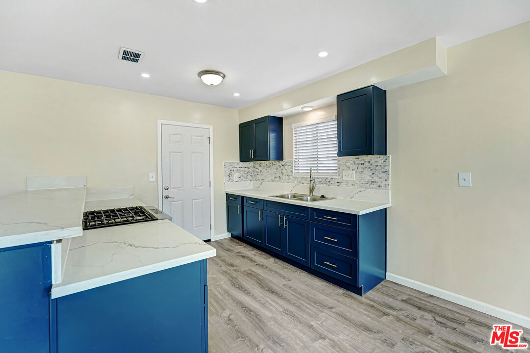 Vacant kitchen with dark blue cabinets, marble-look counters, and a mosaic tile backsplash.