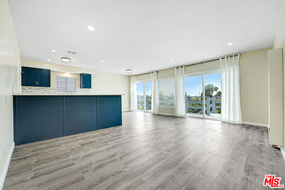 Open-plan kitchen with dark blue cabinetry, gray flooring, and large windows opening to a balcony.
