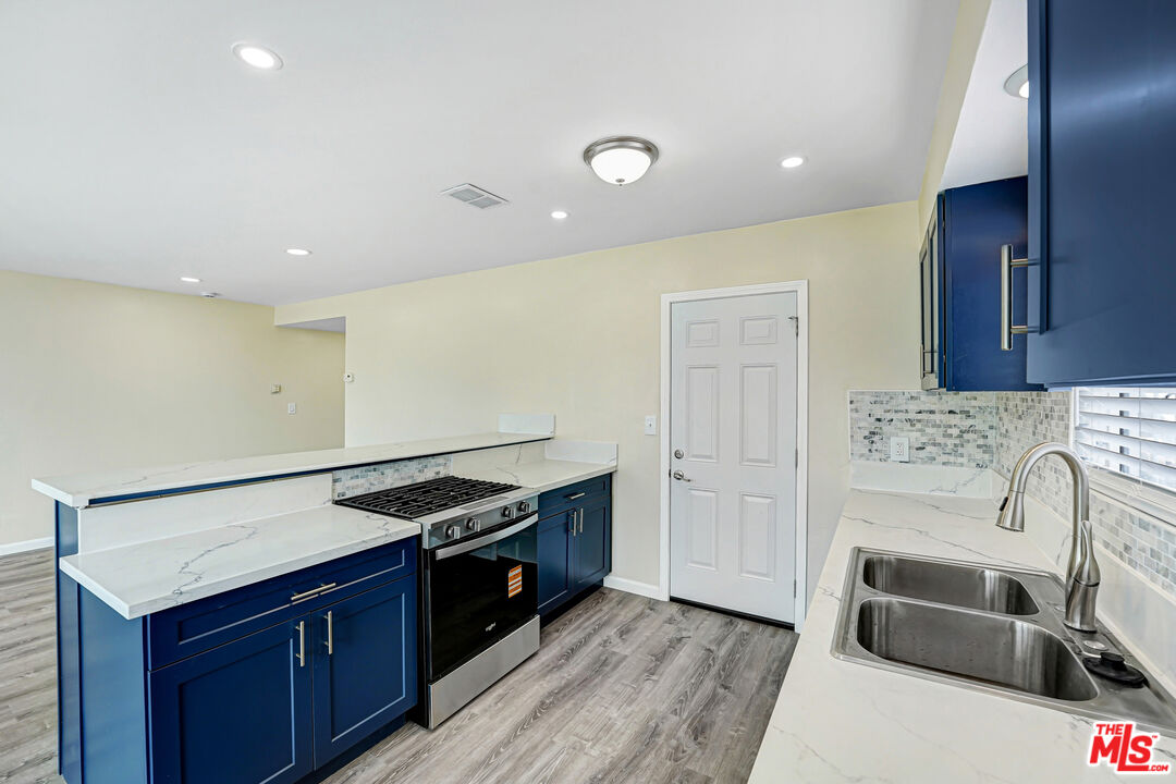 Kitchen with dark blue cabinets, white countertops, a stainless-steel range, and a double sink.