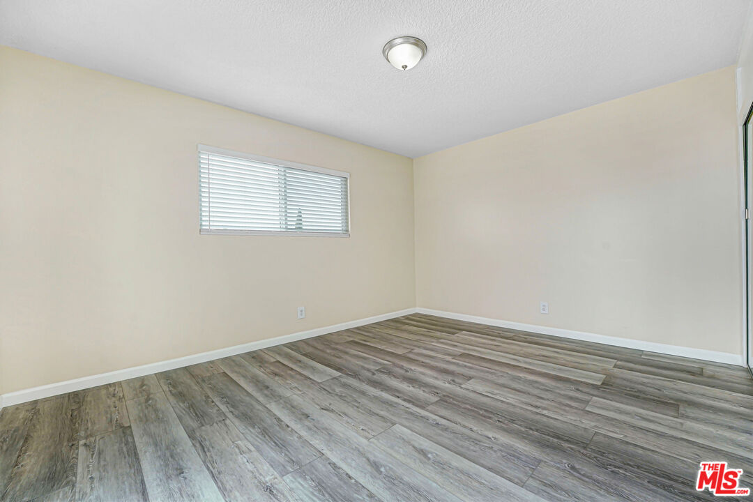 Empty room with gray plank flooring, beige walls, and a high window with blinds.