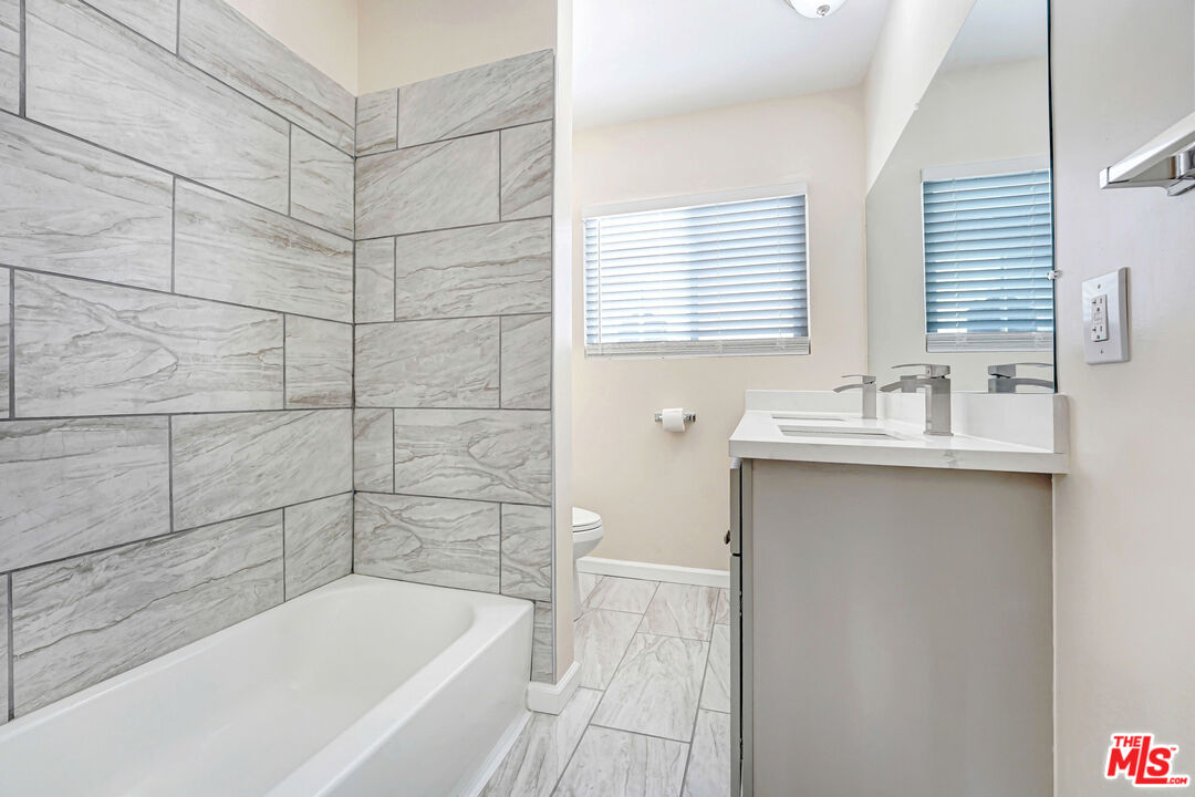 Bathroom with a white tub, gray marble-look tile, and a modern vanity beneath a window.