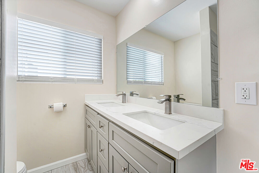 Bathroom double vanity with a white countertop, gray cabinets, and a large mirror.