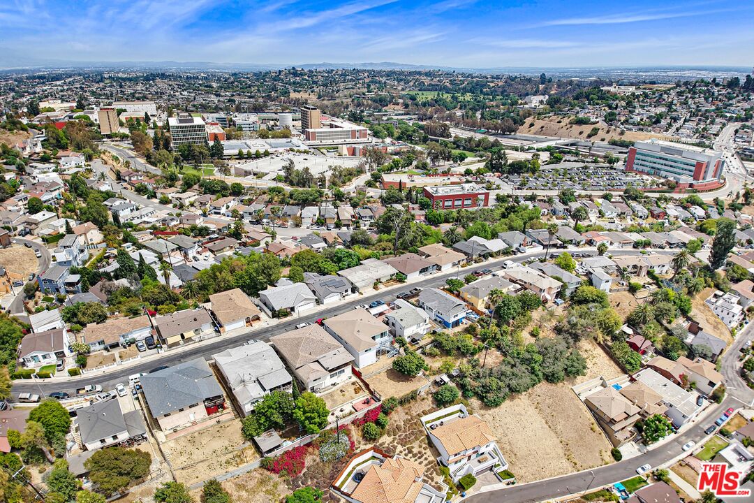 Aerial view over homes toward a large institutional complex and the distant cityscape.