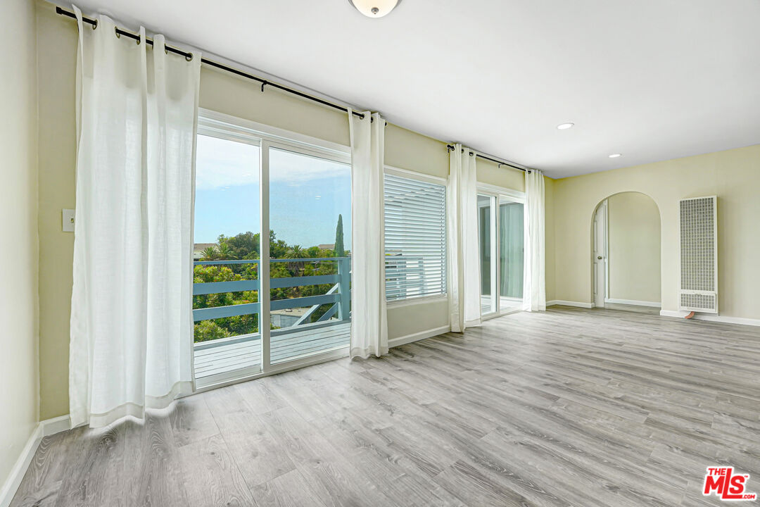 Vacant living room with gray plank flooring, sliding glass doors, and a balcony overlooking leafy trees.