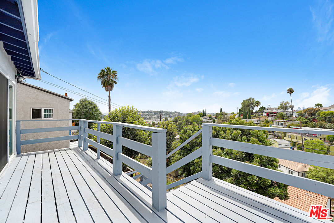 White-railed wooden deck overlooking a leafy neighborhood with palm trees.