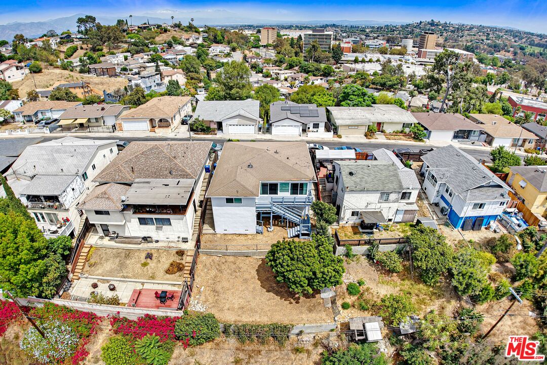 Aerial view of the home, neighboring houses, dry yard, and distant hills.