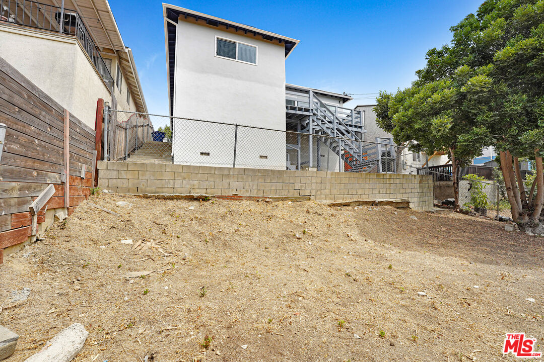 Dry sloping backyard below a block retaining wall and fenced rear structures.