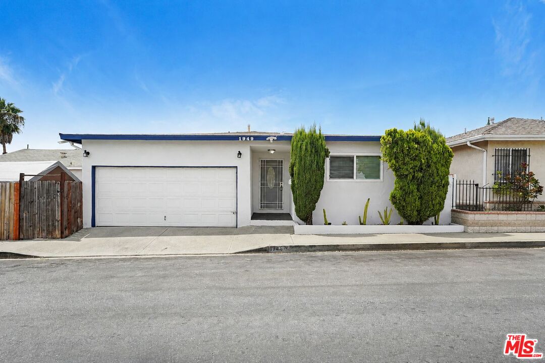 Single-story white house with a large garage, gated entry, and trimmed front shrubs.