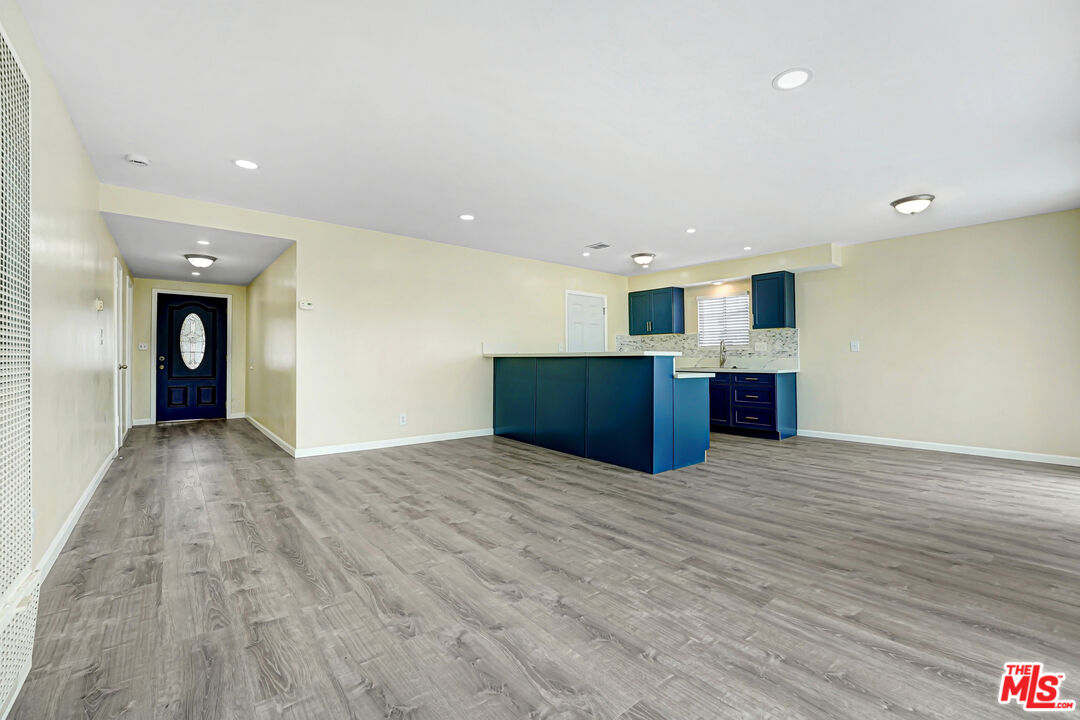 Open living area with gray wood-look floors, dark blue kitchen cabinets, and a peninsula beside the entry hall.
