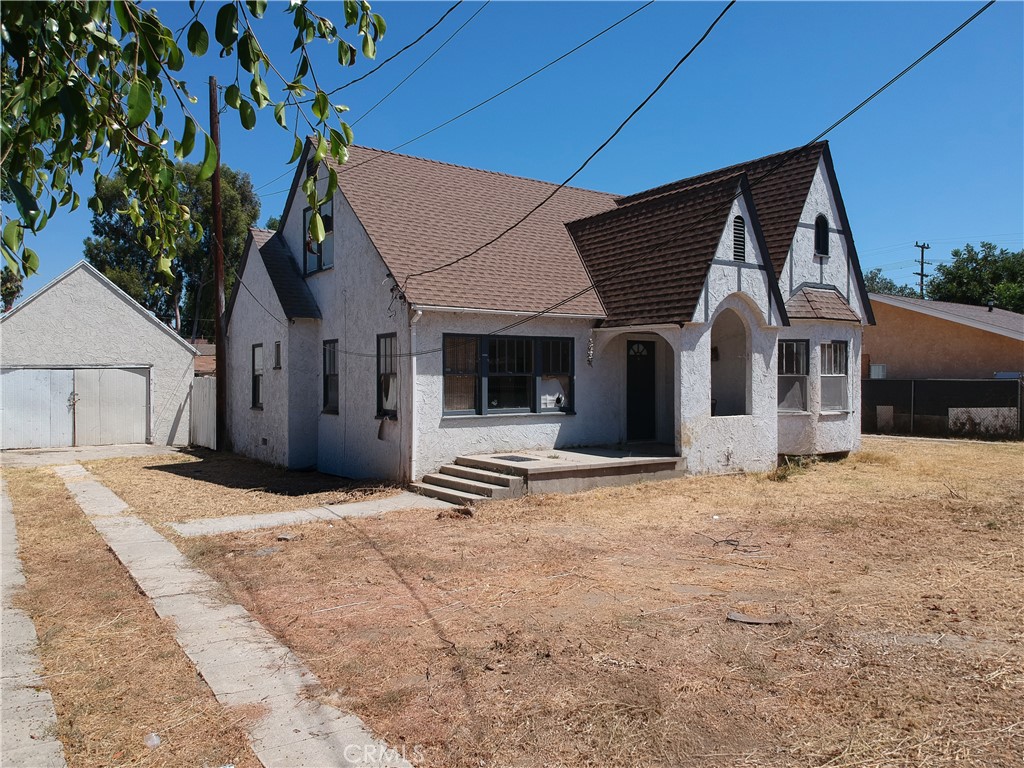 White stucco house with steep gabled roofs and arched entryways in a dry yard.