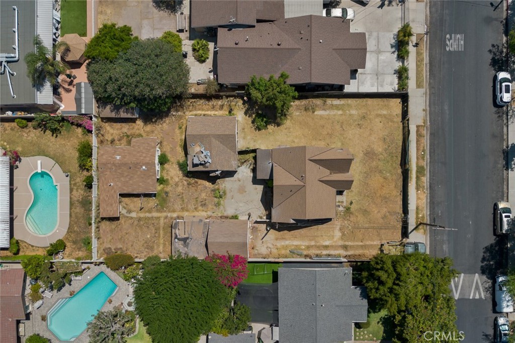 Aerial view of a fenced property with several small structures and a dry yard beside the street.