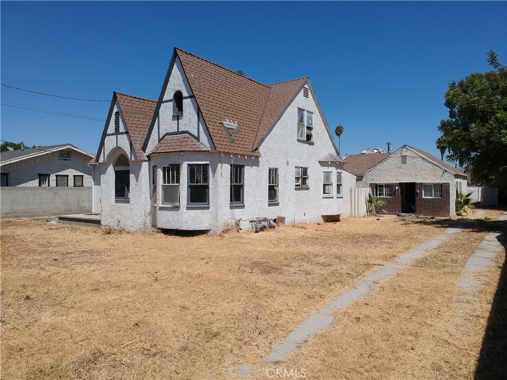White stucco house with steep brown gabled roofs, dry yard, and detached brick garage.