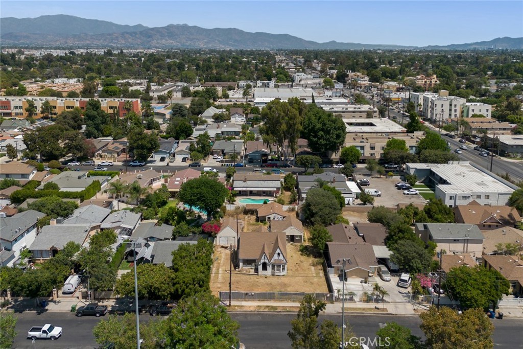 Aerial view of a detached house on a bare lot, with neighborhood homes and mountains beyond.