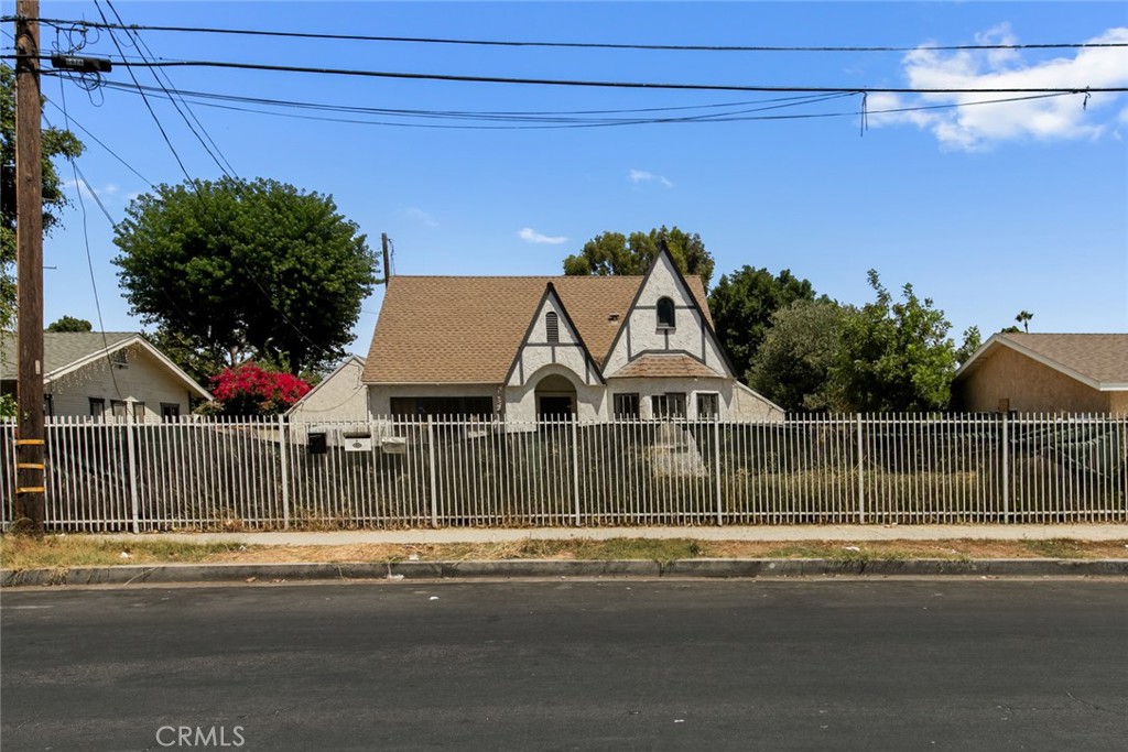 Tudor-style house behind a tall metal fence, viewed from across the street.