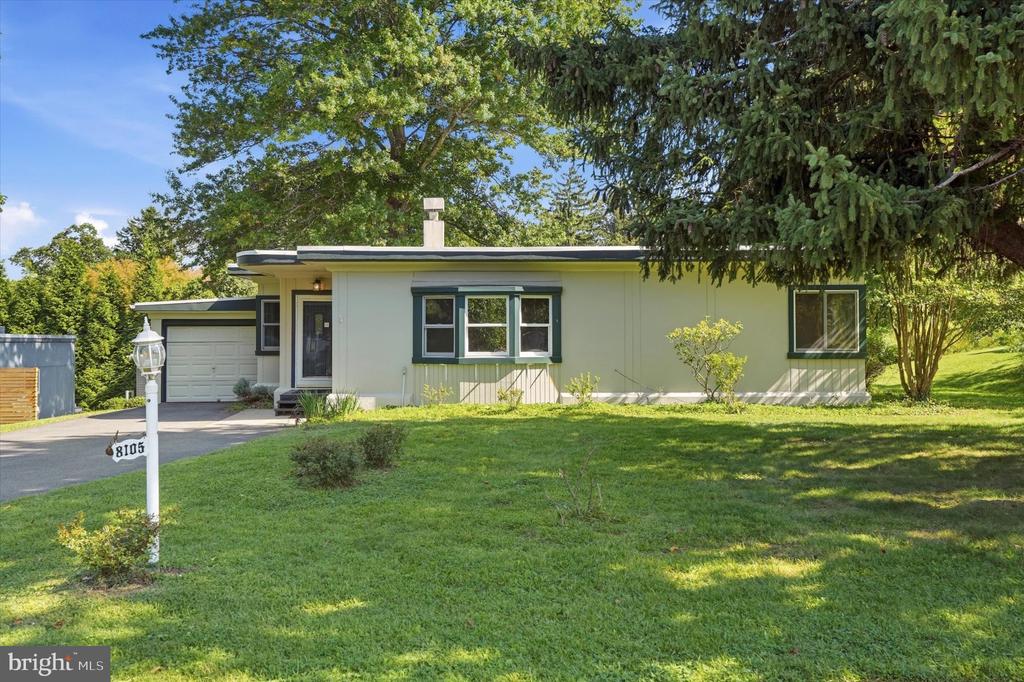 Single-story home with attached garage, broad lawn, and mature trees.