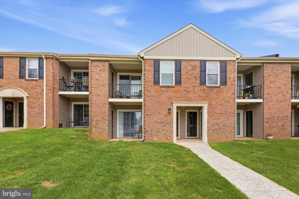 Brick residential building with balconies, a central entrance, and a walkway across the lawn.