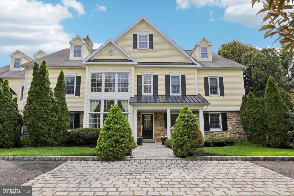 Pale-yellow two-story house with black shutters, stone facade, and a paved front drive.