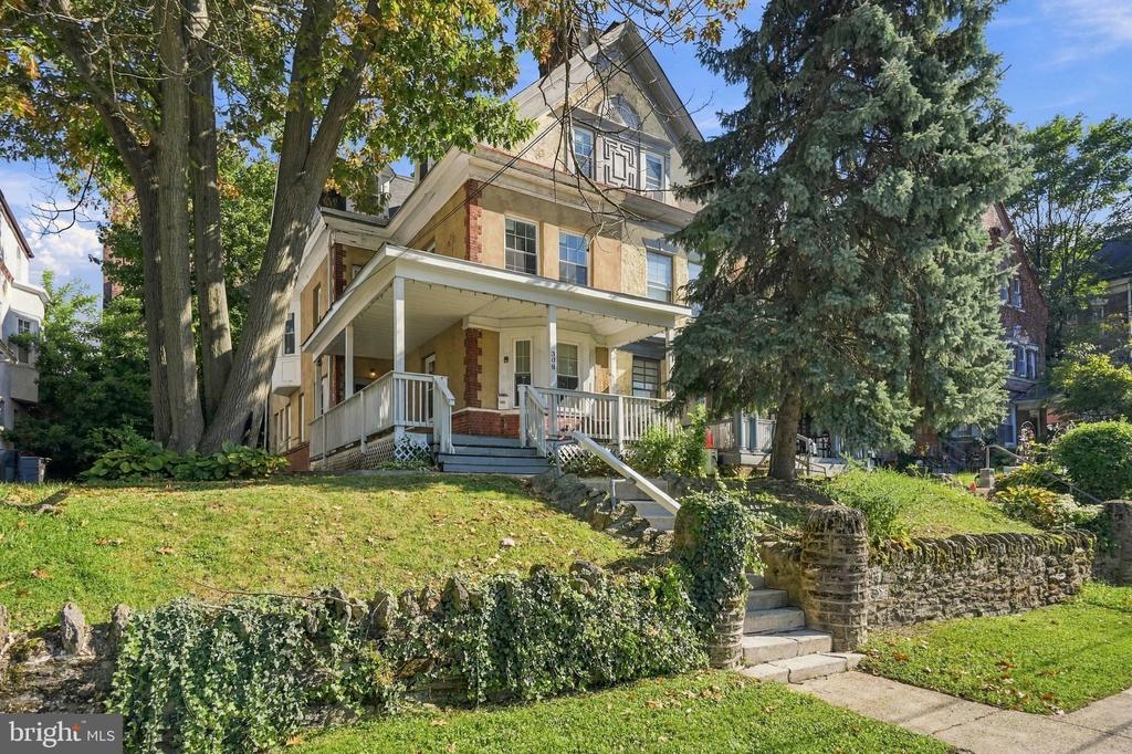 Multi-story Philadelphia home with a broad porch, stone retaining wall, and mature trees.