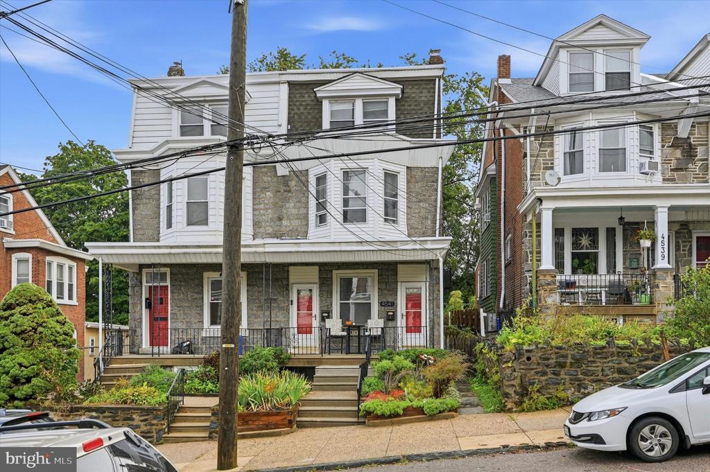 Stone-and-siding Philadelphia home with a covered porch, red doors, and planted front garden.