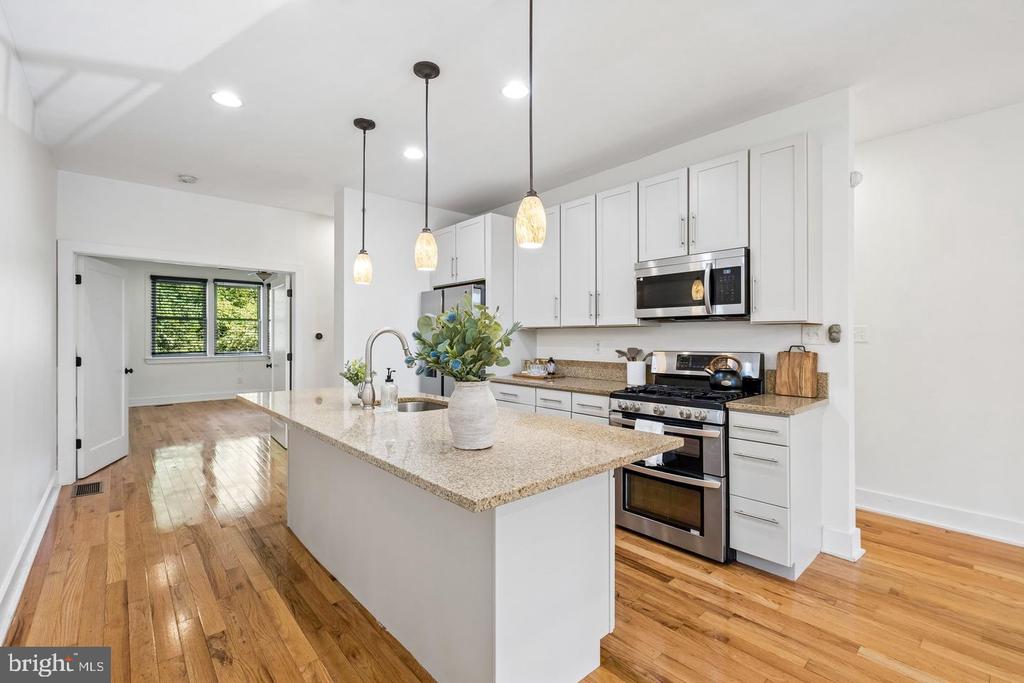 Kitchen with a large granite island, white cabinets, stainless steel appliances, and hardwood floors.