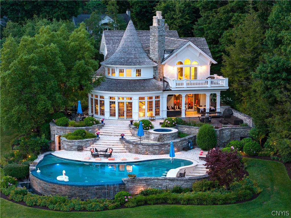 White shingle-style home with a turret, tiered stone terraces, and a curved swimming pool.