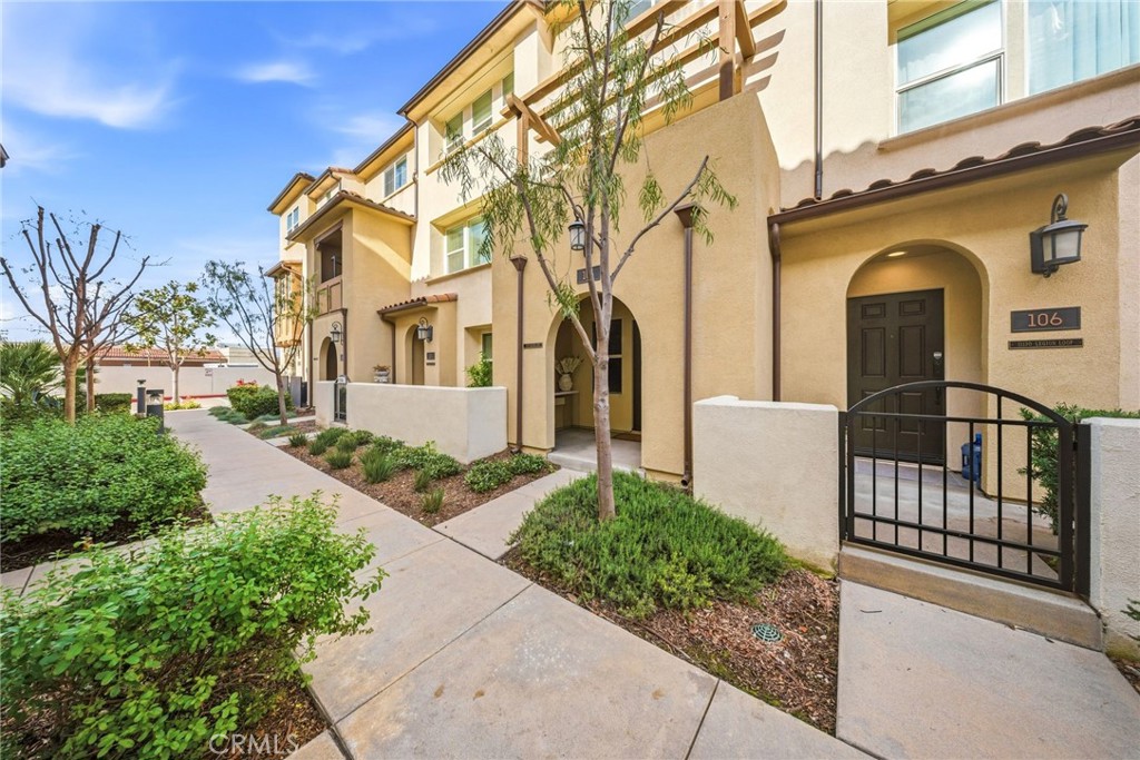 Beige townhouse exterior with arched entryways, gated patio, and landscaped walkway.