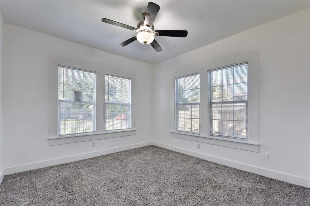 Empty bedroom with gray carpet, ceiling fan, and four windows with blinds.