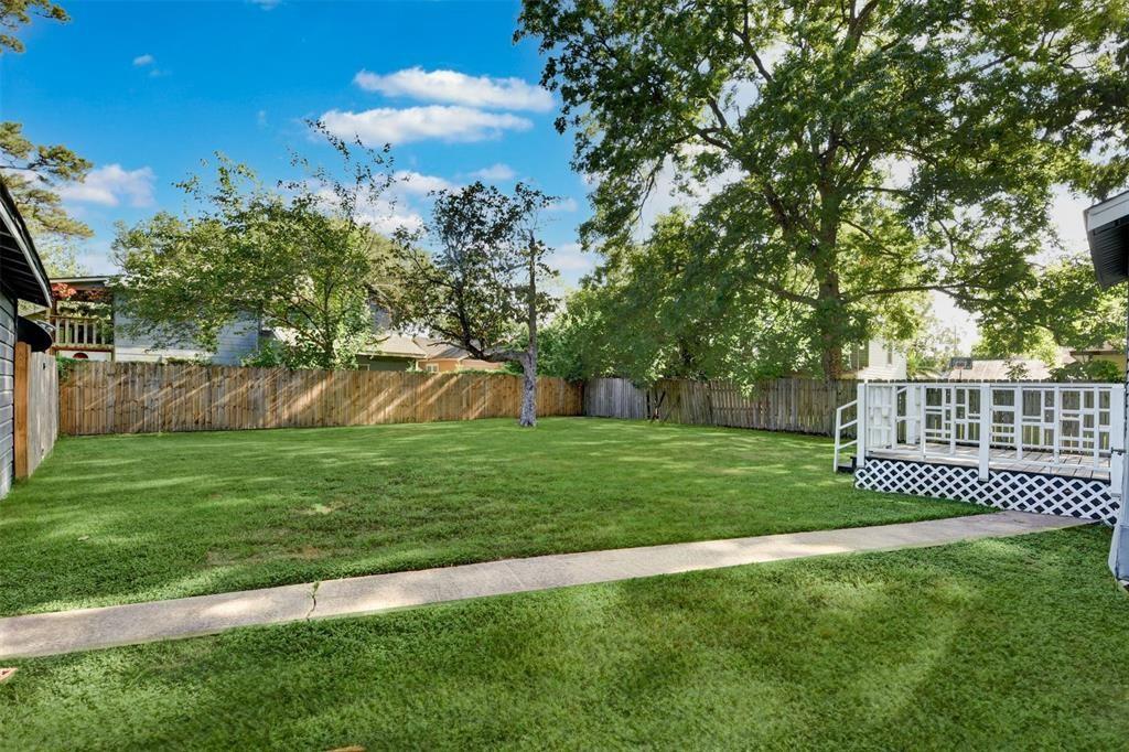 Fenced backyard with a broad lawn, mature shade trees, and a small white raised deck.