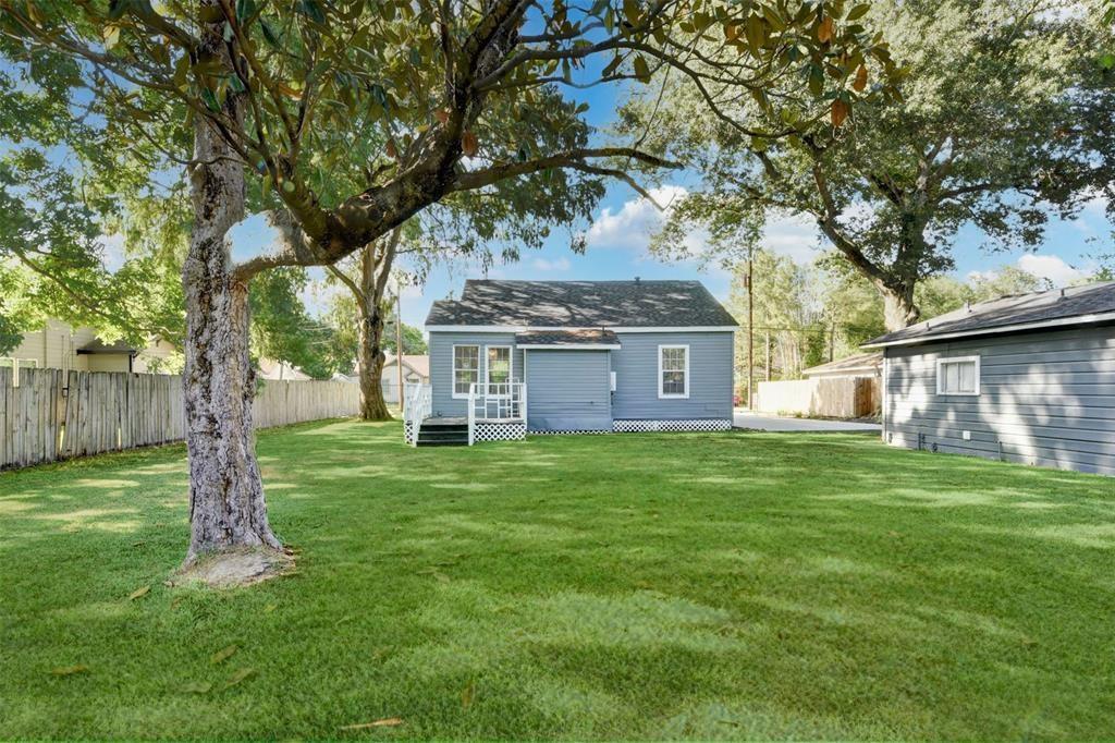 Blue-gray single-story house beyond a broad lawn, shaded by mature trees.