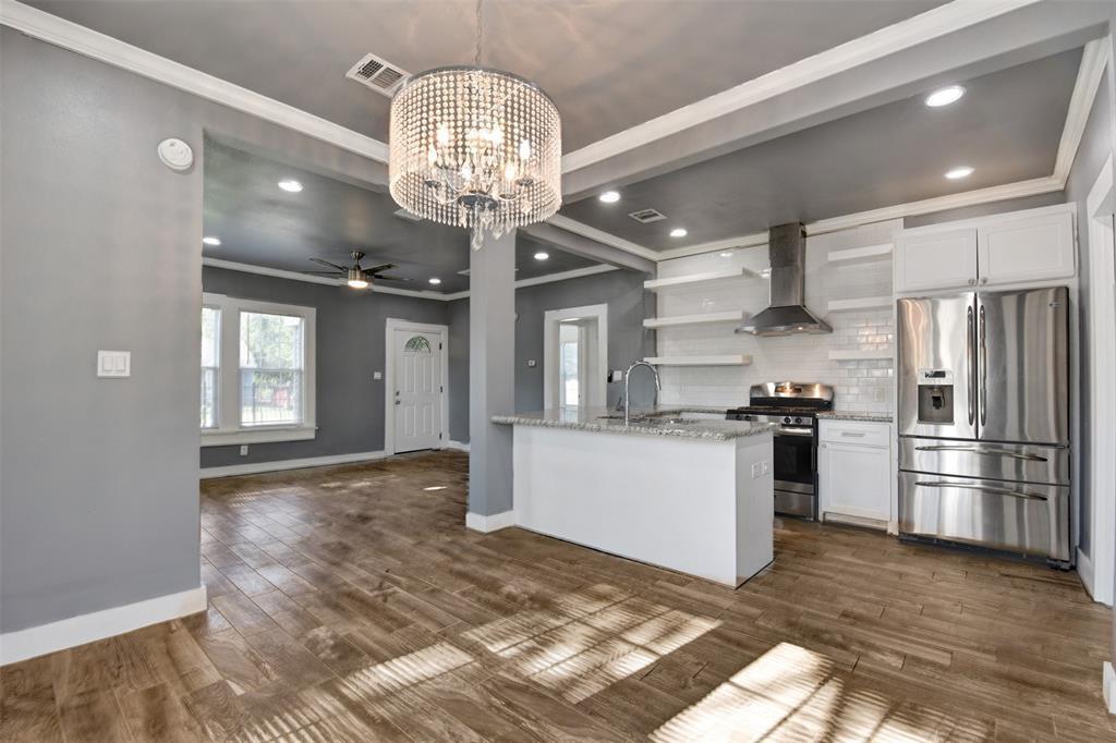Open kitchen and living area with a white island, stainless steel appliances, and crystal chandelier.