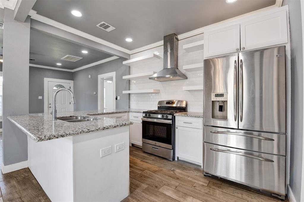 Kitchen with a granite island, white cabinetry, open shelves, and stainless-steel appliances.