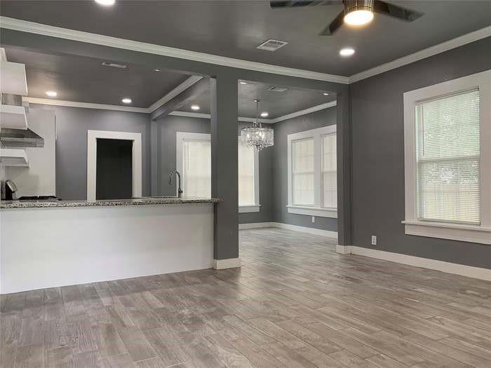 Open kitchen and living area with a granite breakfast bar, gray walls, and wood-look tile flooring.