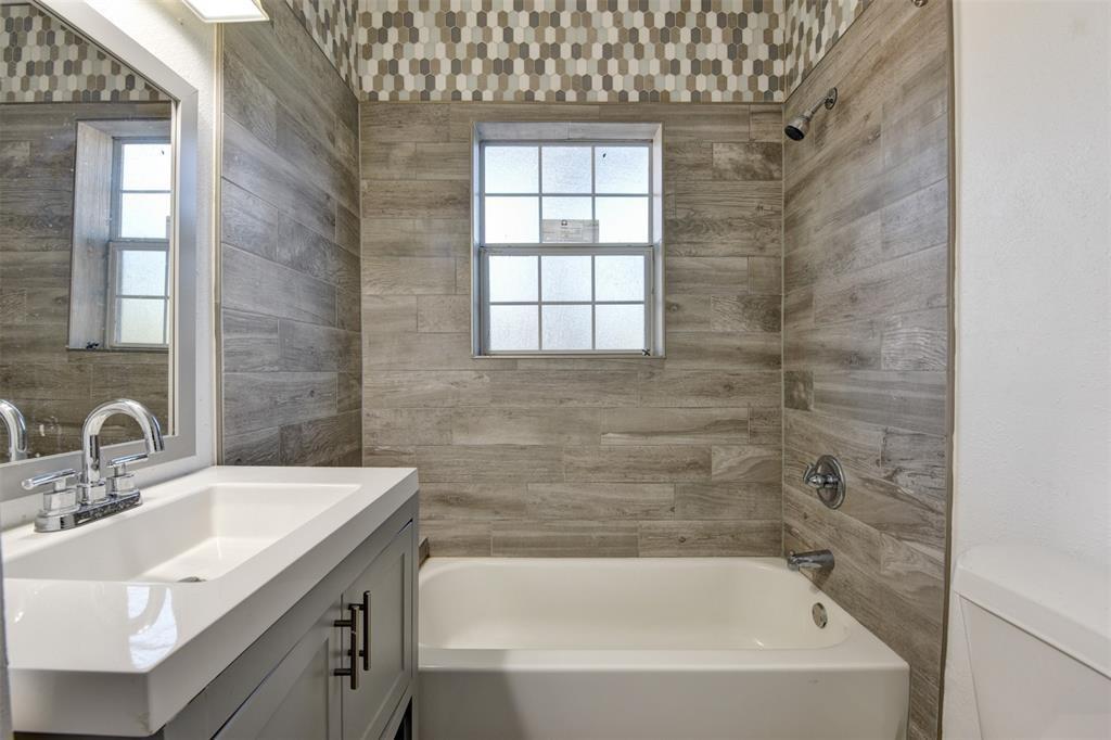 Bathroom with a white tub, gray tile walls, patterned accent tile, and a gray vanity.