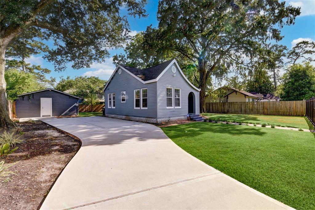 Gray-blue house with a wide driveway, detached outbuilding, and mature shade trees.