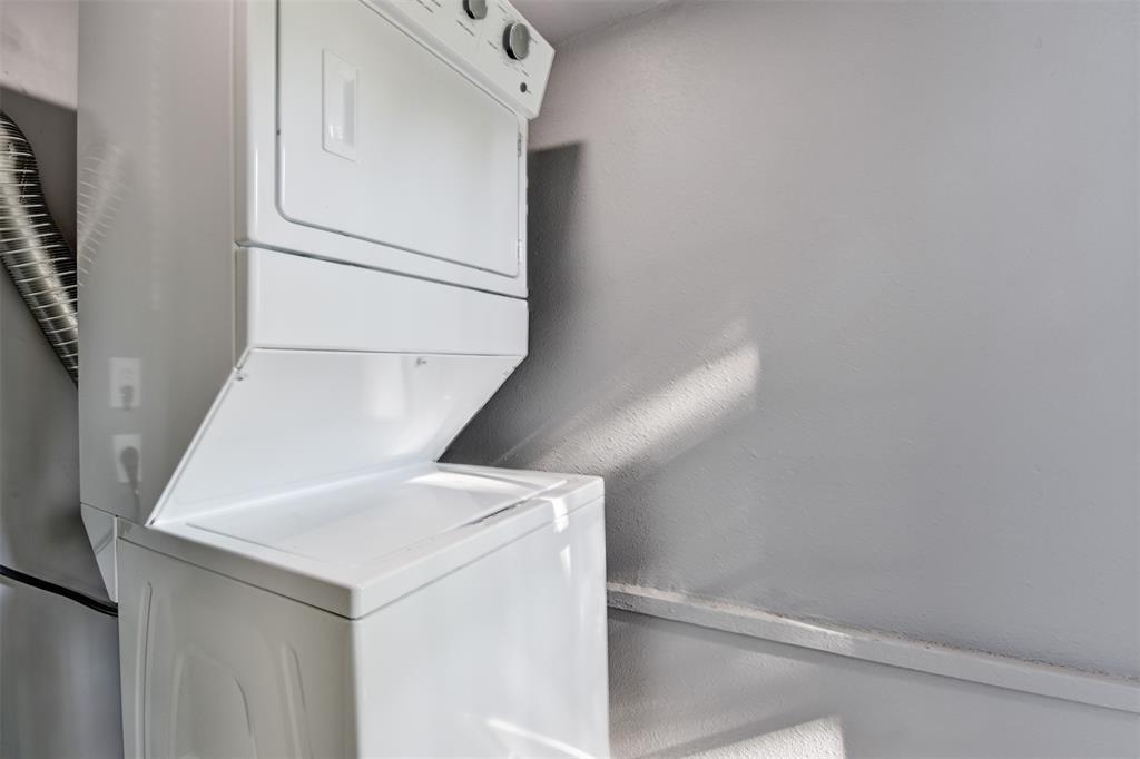 Stacked white washer and dryer in a small laundry area with gray walls.