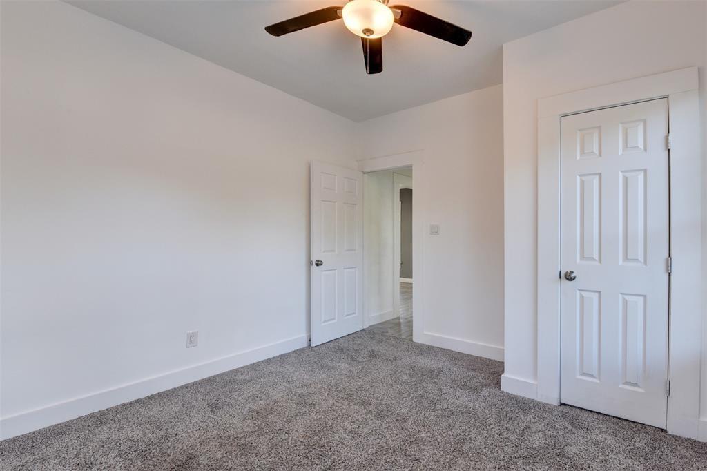 Empty bedroom with gray carpet, a ceiling fan, and two white paneled doors.