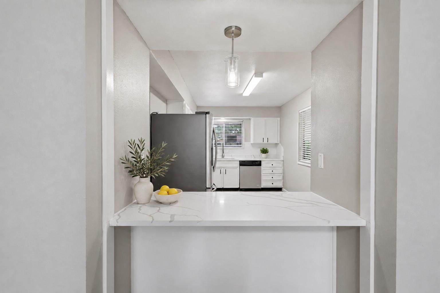 Bright kitchen with a large veined island, white cabinets, and stainless steel refrigerator.