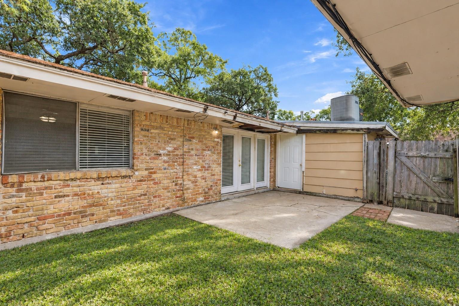 Rear of a brick house with French doors opening onto a concrete patio and lawn.