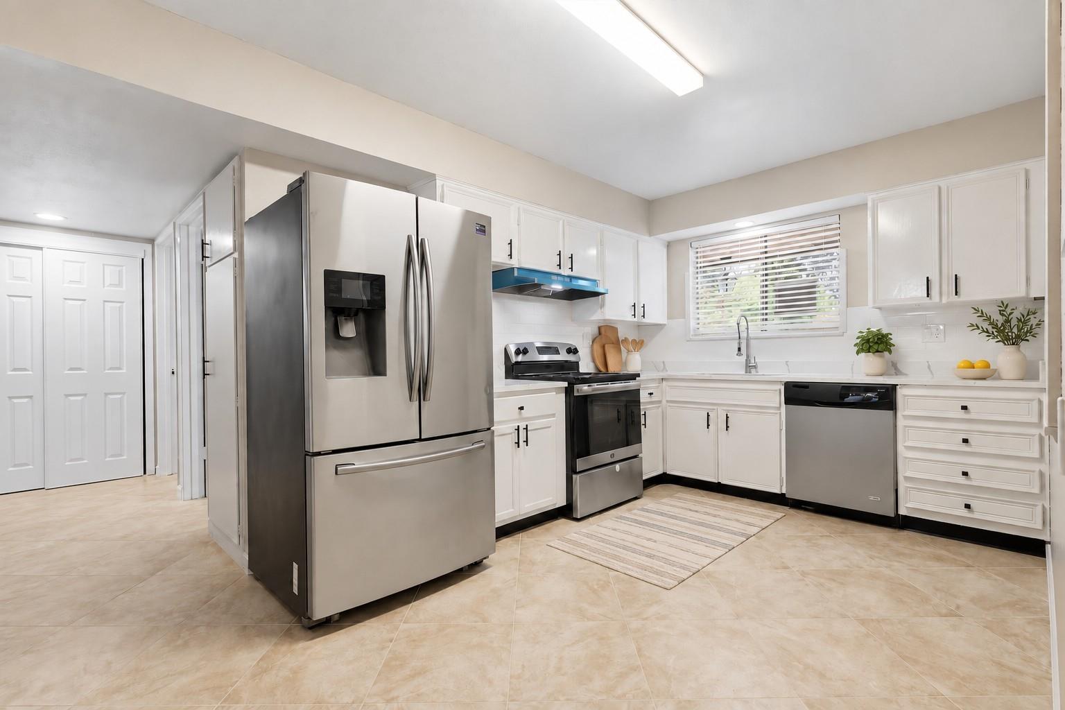 Bright kitchen with white cabinets, stainless steel appliances, and a window above the sink.